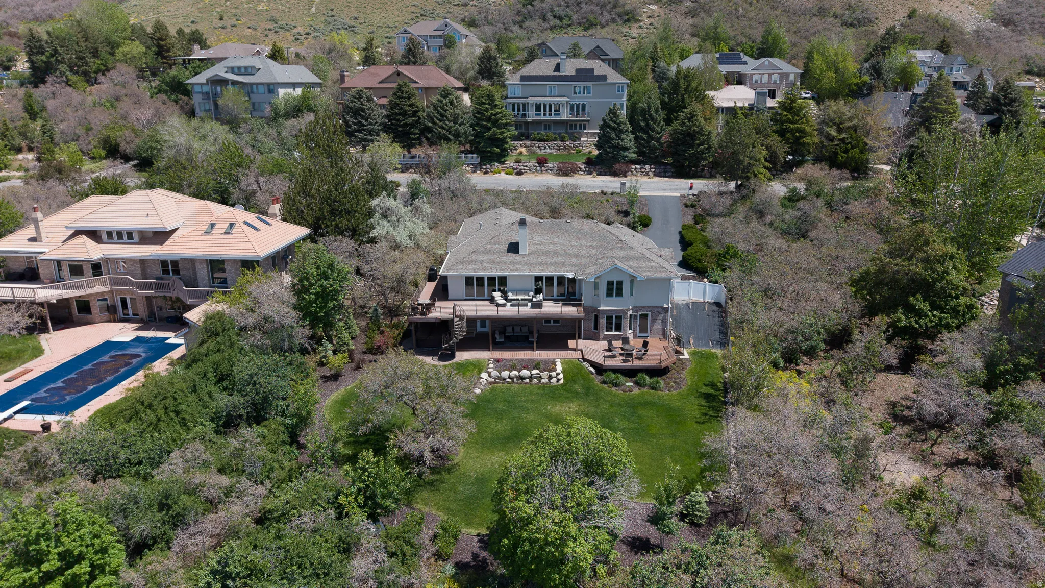 Rear exterior featuring a multi-level deck, lower patio with built-in fire pit, and a landscaped lawn