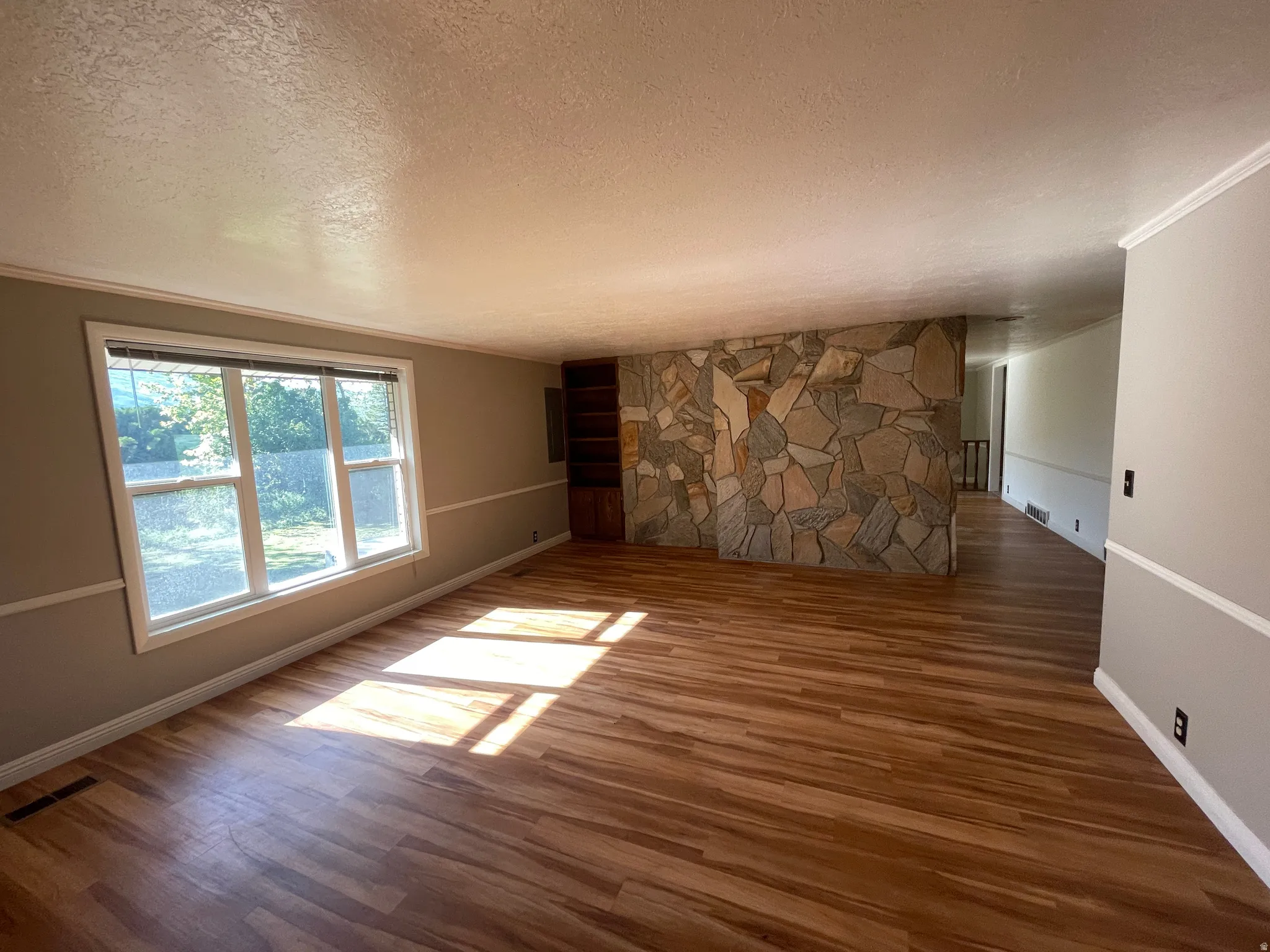 Spacious interior featuring wood-finish flooring, a stone-accented wall, and built-in shelving