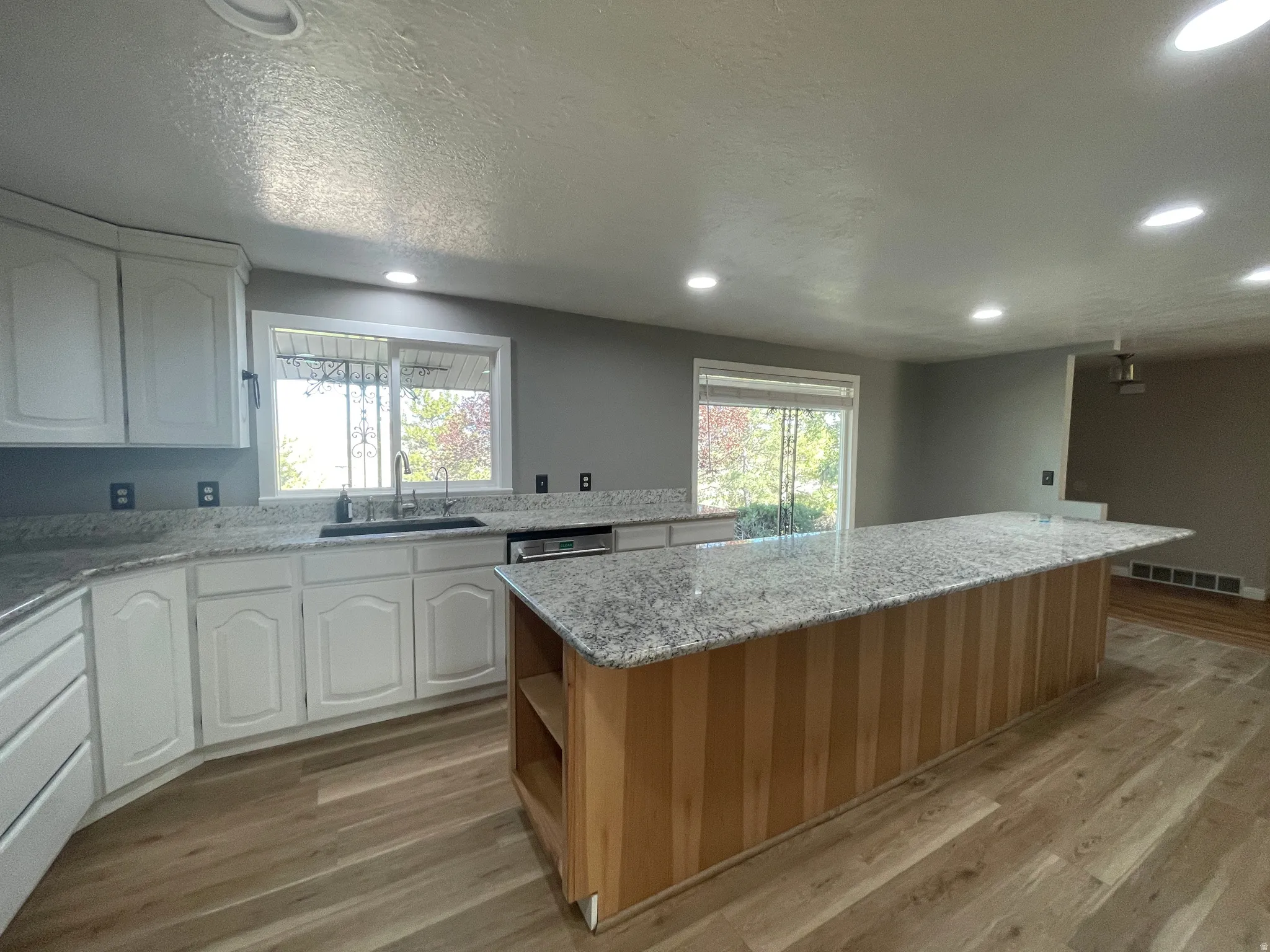 Kitchen featuring a large central island with a light wood base, granite countertops, white cabinetry, wood-finish flooring, and recessed lighting