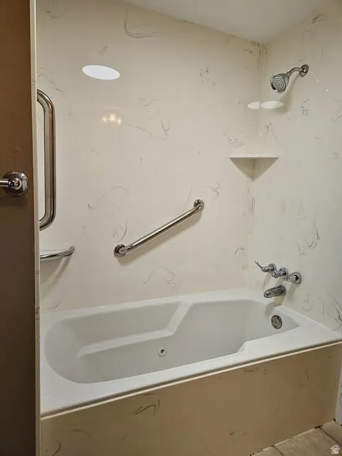 Bathtub and shower combination featuring a white tub, chrome fixtures, and a light-toned, subtly patterned surround