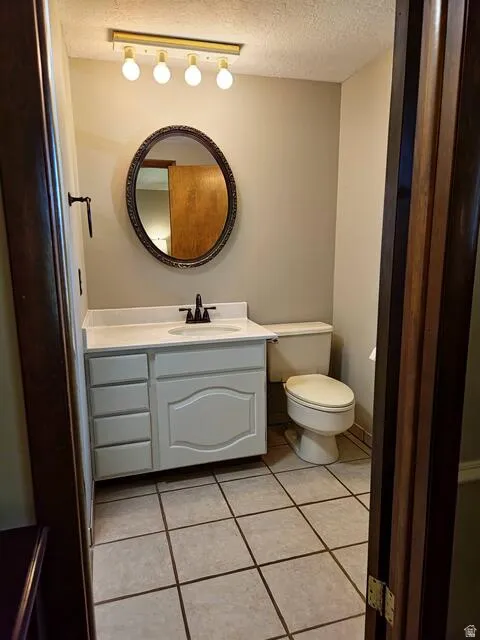 Bathroom featuring a white vanity with integrated sink, coordinating commode, gold-toned four-bulb light fixture, and an ornate oval mirror