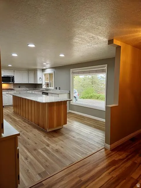 Spacious kitchen featuring an extended wood-finish island with a stone-finish countertop, white cabinetry, recessed lighting, and wood-finish flooring