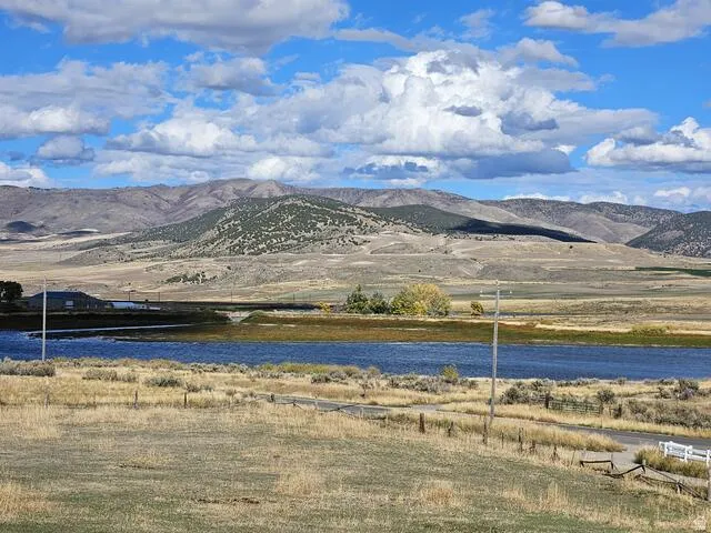 Expansive rural landscape featuring a body of water, distant mountains, and a clear sky with clouds