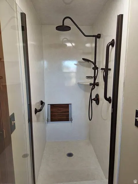 Walk-in shower featuring a rainfall showerhead, handheld shower fixture, and a folding wood-slat bench