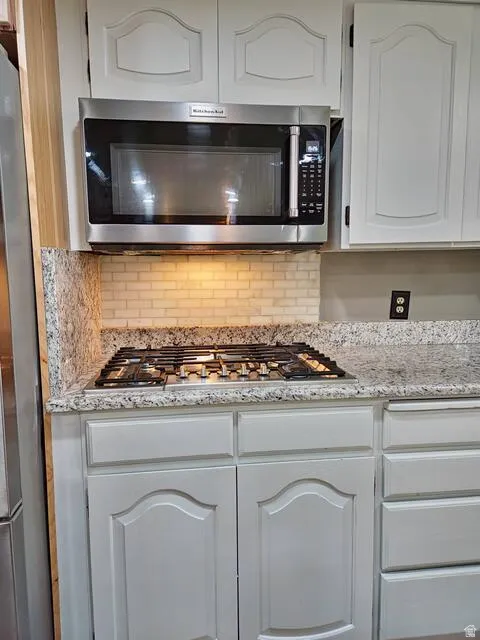Kitchen featuring white upper and lower cabinetry, stainless steel over-the-range microwave, built-in gas cooktop, granite countertops, and a tiled backsplash
