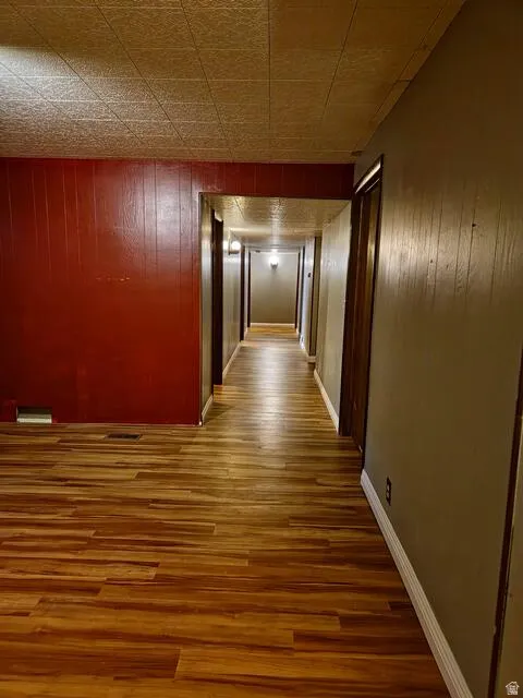 Hallway featuring wood-finish flooring, a textured ceiling, a red accent wall, and multiple doorways