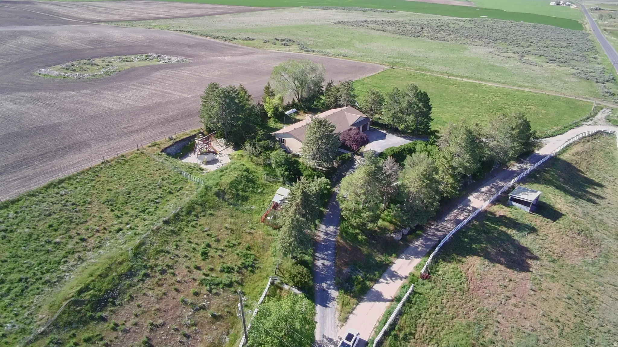 Aerial perspective showcasing a single-story dwelling surrounded by agricultural land and mature trees