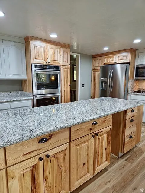 Kitchen featuring a central island with granite countertops, natural wood cabinetry, stainless steel double wall ovens, a stainless steel refrigerator, and recessed lighting