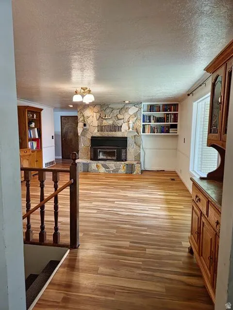 Spacious room featuring wood-finish flooring, a stone-clad fireplace, and built-in shelving