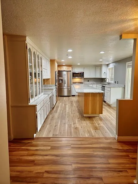 Kitchen featuring wood-finish flooring, recessed lighting, a central island with wood paneling, white cabinetry, and stainless steel appliances