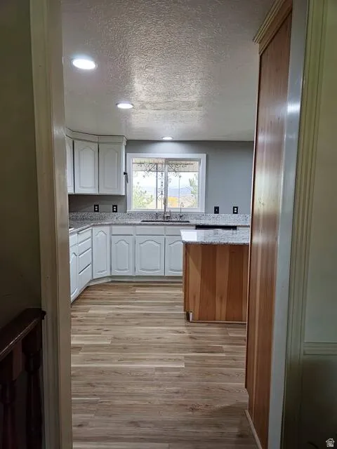 Kitchen featuring white cabinetry, light-toned wood-finish flooring, recessed lighting, and a window above the sink