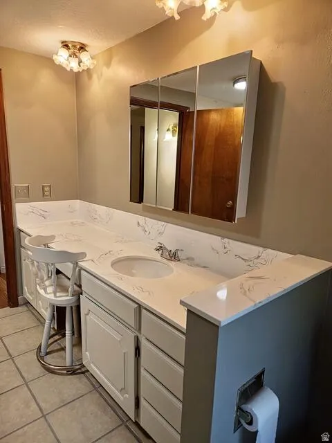 Bathroom featuring a vanity with a white countertop and integrated sink, a three-panel mirrored medicine cabinet, built-in cabinetry, and tile flooring