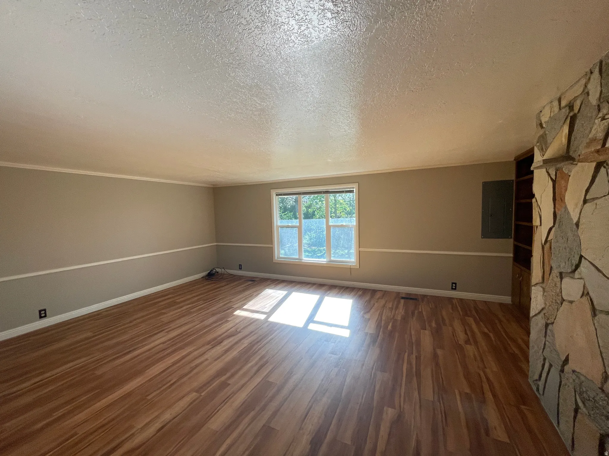 Spacious room featuring wood-finish flooring, a multi-pane window, and a stone-clad wall with built-in shelving