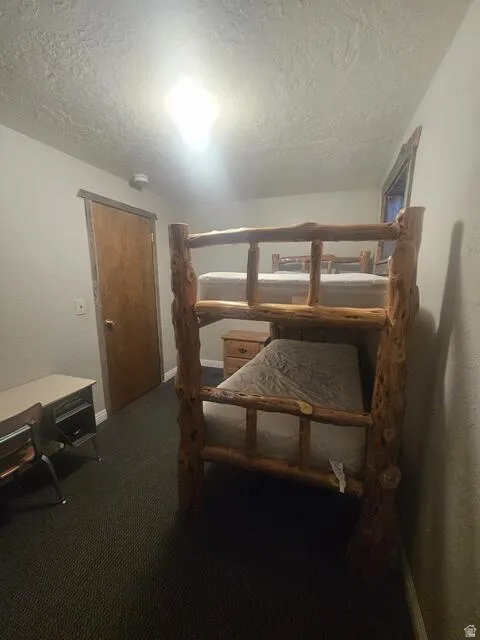 Room featuring a rustic wood-frame bunk bed, textured ceilings, a warm wood-tone door, and dark patterned carpeting