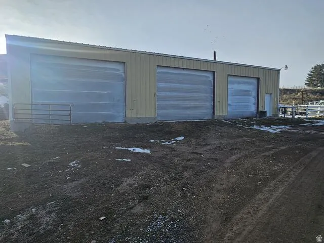 Metal-sided utility building featuring three roll-up doors, a pedestrian entry door, and a full-length gutter system