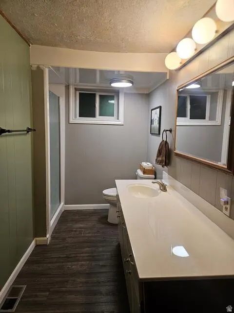 Bathroom featuring a spacious vanity with an integrated sink, wood-finish flooring, a wall-mounted light fixture, a mirrored medicine cabinet, and a shower enclosure