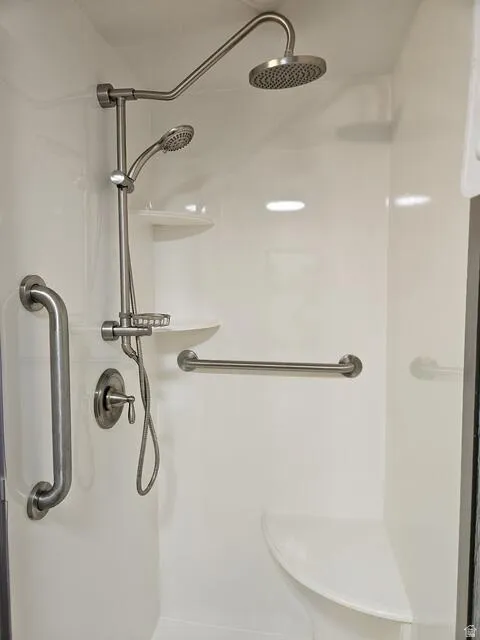 Shower enclosure featuring a rain shower head, handheld shower, integrated shelving, built-in seating, and grab bars