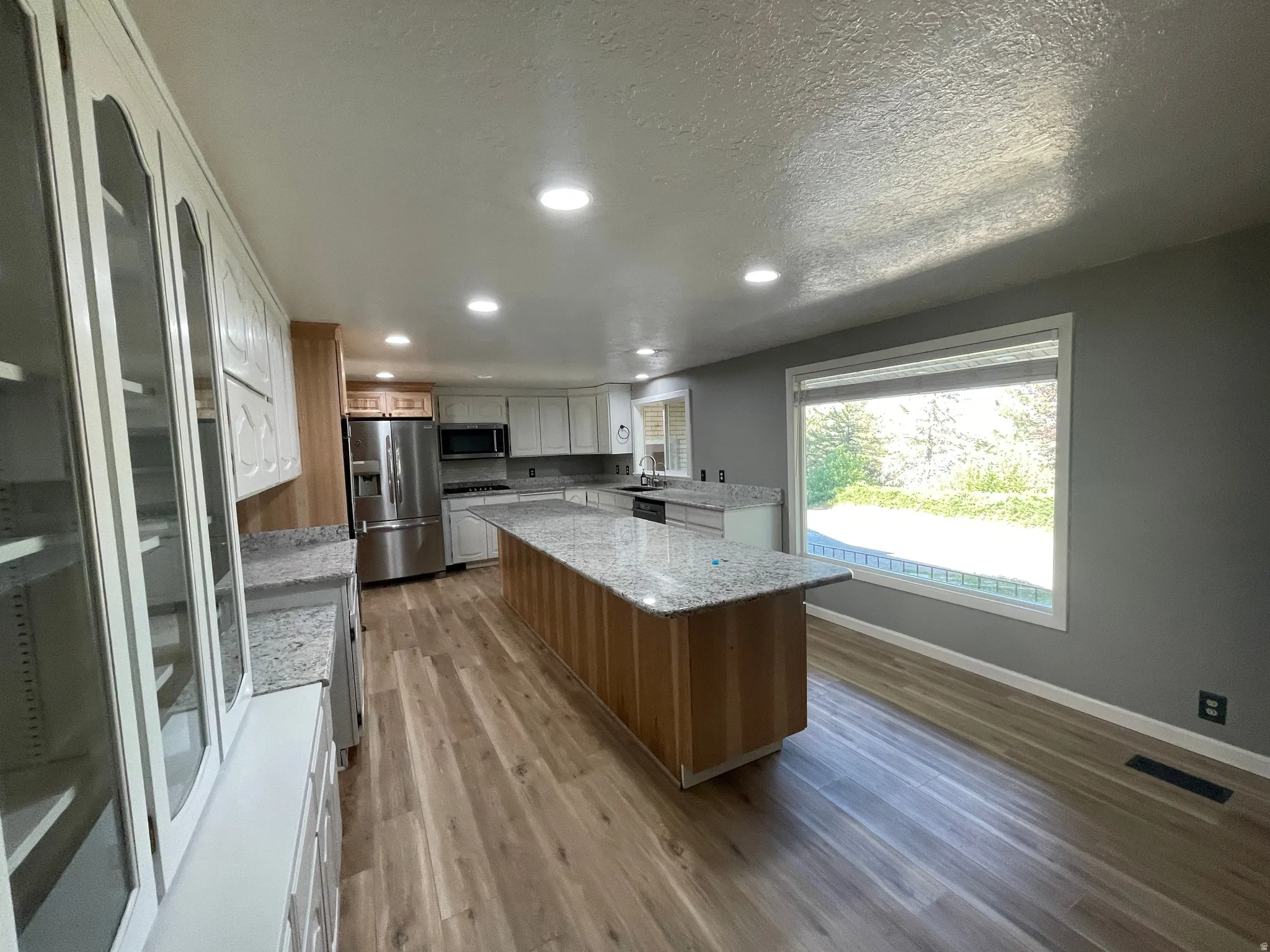Spacious kitchen featuring an extended island with a light-toned wood finish, granite-style countertops, stainless steel appliances, recessed lighting, and wood-finish flooring