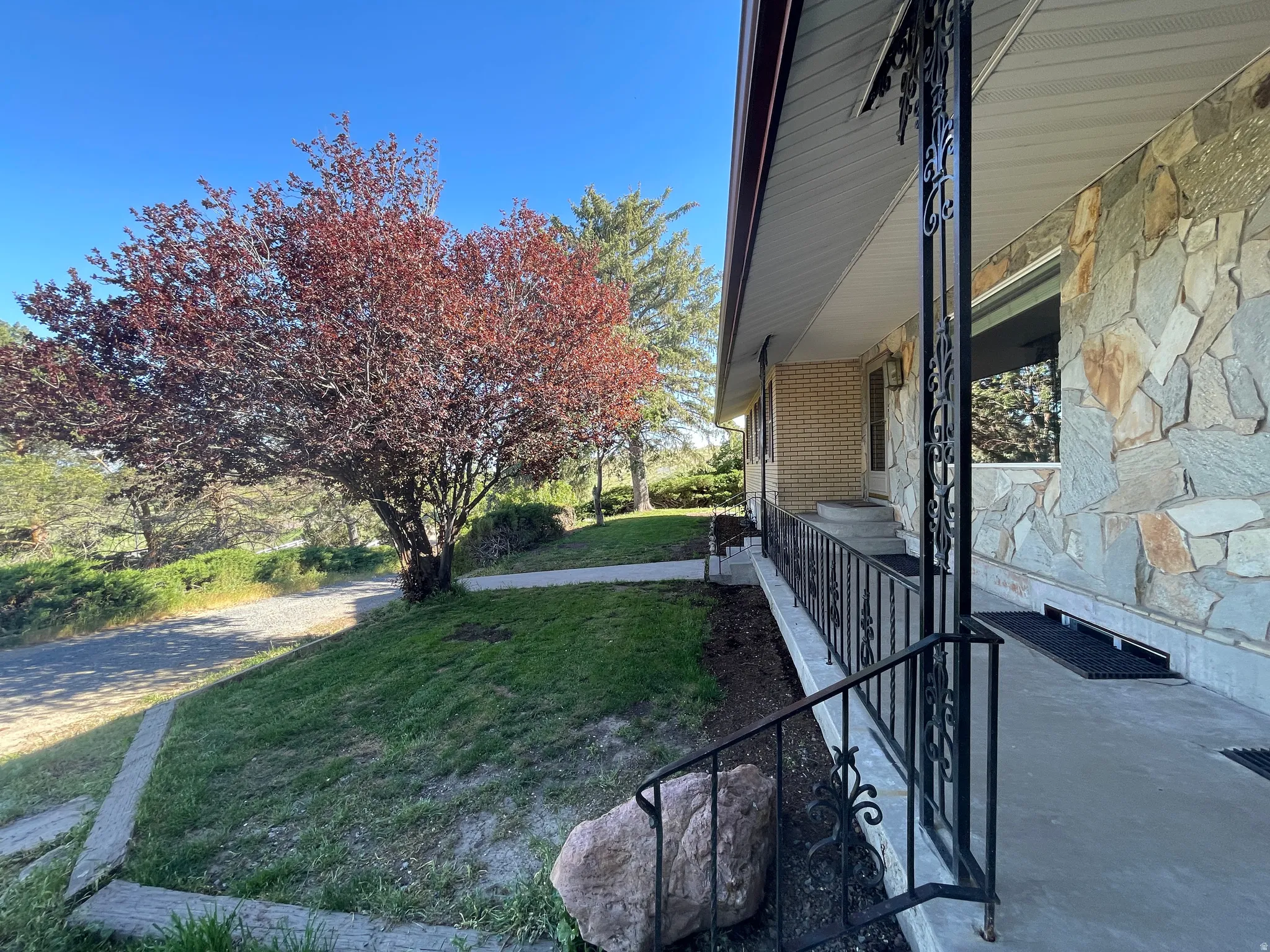 Stone veneer exterior with a concrete front porch, ornamental black metal railings, and a mature tree providing shade