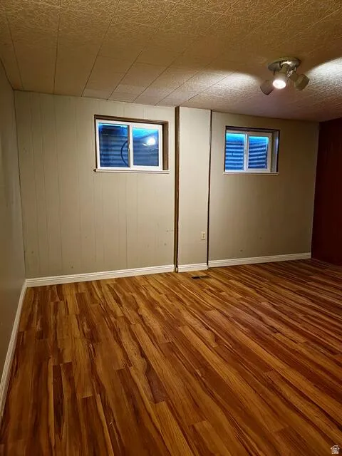 Room featuring wood-finish flooring, two windows with grates, track lighting, and paneled walls