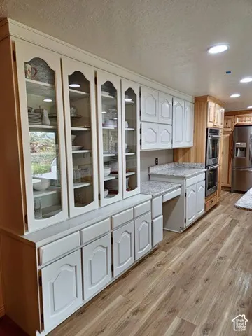 Kitchen featuring white cabinetry with glass display doors, recessed lighting, wood-finish flooring, light-toned countertops, and built-in double ovens