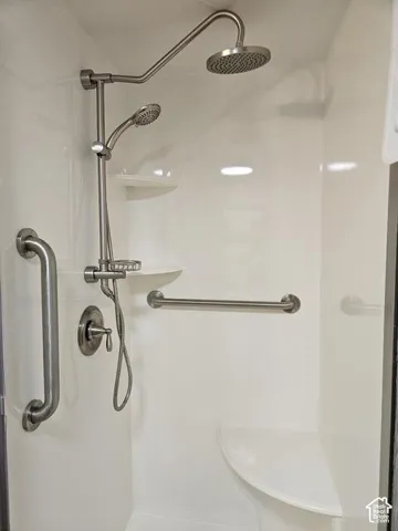 Shower enclosure featuring a rain shower head, handheld shower, integrated shelving, built-in seating, and grab bars