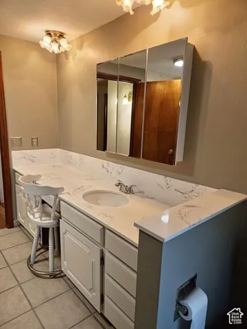 Bathroom featuring a vanity with a white countertop and integrated sink, a three-panel mirrored medicine cabinet, built-in cabinetry, and tile flooring