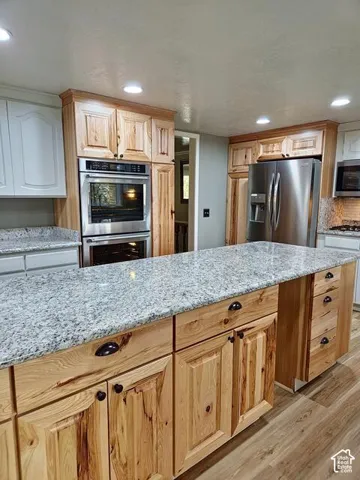 Kitchen featuring a central island with granite countertops, natural wood cabinetry, stainless steel double wall ovens, a stainless steel refrigerator, and recessed lighting