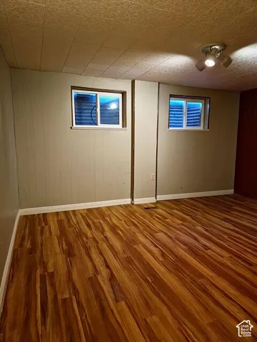 Room featuring wood-finish flooring, two windows with grates, track lighting, and paneled walls