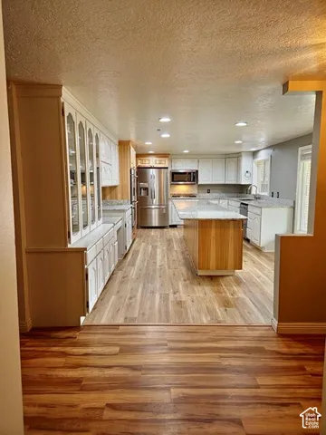 Kitchen featuring wood-finish flooring, recessed lighting, a central island with wood paneling, white cabinetry, and stainless steel appliances