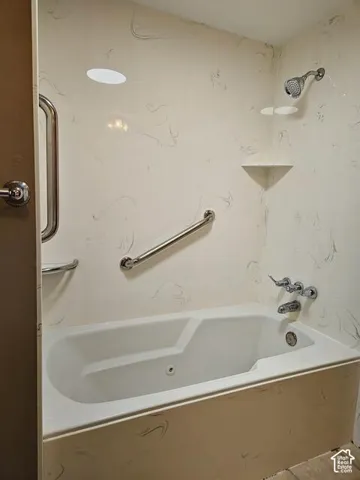 Bathtub and shower combination featuring a white tub, chrome fixtures, and a light-toned, subtly patterned surround