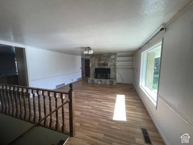 Spacious living area featuring wood-finish flooring, a stone fireplace with hearth, a large picture window, built-in shelving, and a classic wooden staircase railing
