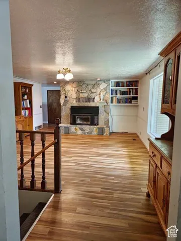 Spacious room featuring wood-finish flooring, a stone-clad fireplace, and built-in shelving