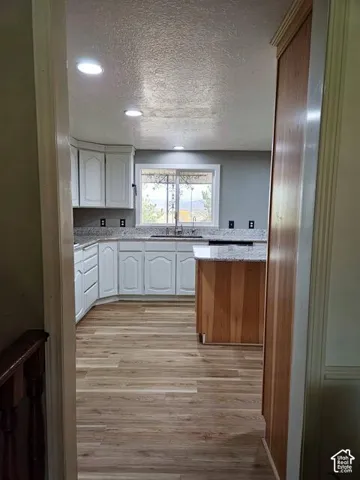 Kitchen featuring white cabinetry, light-toned wood-finish flooring, recessed lighting, and a window above the sink