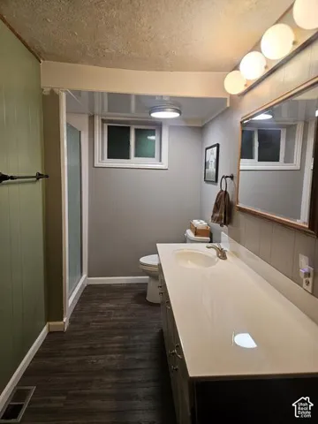 Bathroom featuring a spacious vanity with an integrated sink, wood-finish flooring, a wall-mounted light fixture, a mirrored medicine cabinet, and a shower enclosure
