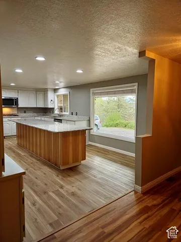 Spacious kitchen featuring an extended wood-finish island with a stone-finish countertop, white cabinetry, recessed lighting, and wood-finish flooring