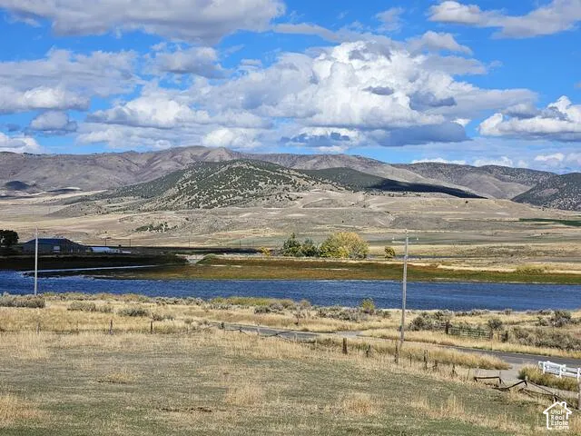 Expansive rural landscape featuring a body of water, distant mountains, and a clear sky with clouds
