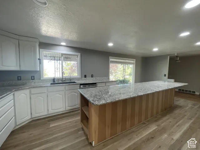 Kitchen featuring a large central island with a light wood base, granite countertops, white cabinetry, wood-finish flooring, and recessed lighting