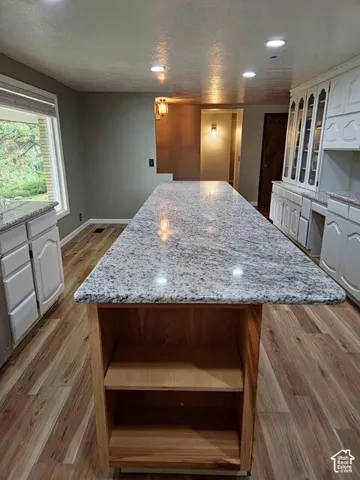 Expansive kitchen island featuring a light-toned granite countertop and natural wood-finish base with open shelving