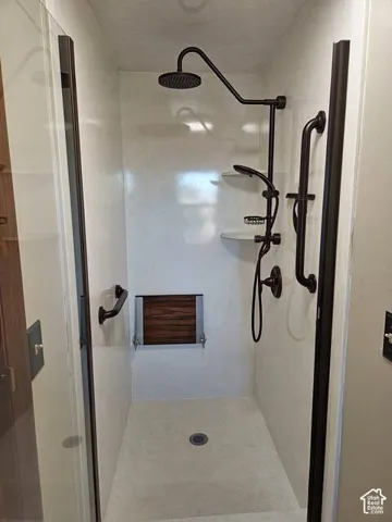 Walk-in shower featuring a rainfall showerhead, handheld shower fixture, and a folding wood-slat bench