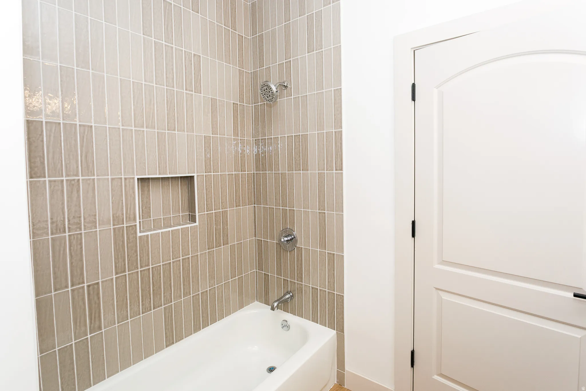 Bathtub with floor-to-ceiling vertical tile surround, integrated shower niche, chrome shower head, and chrome tub faucet