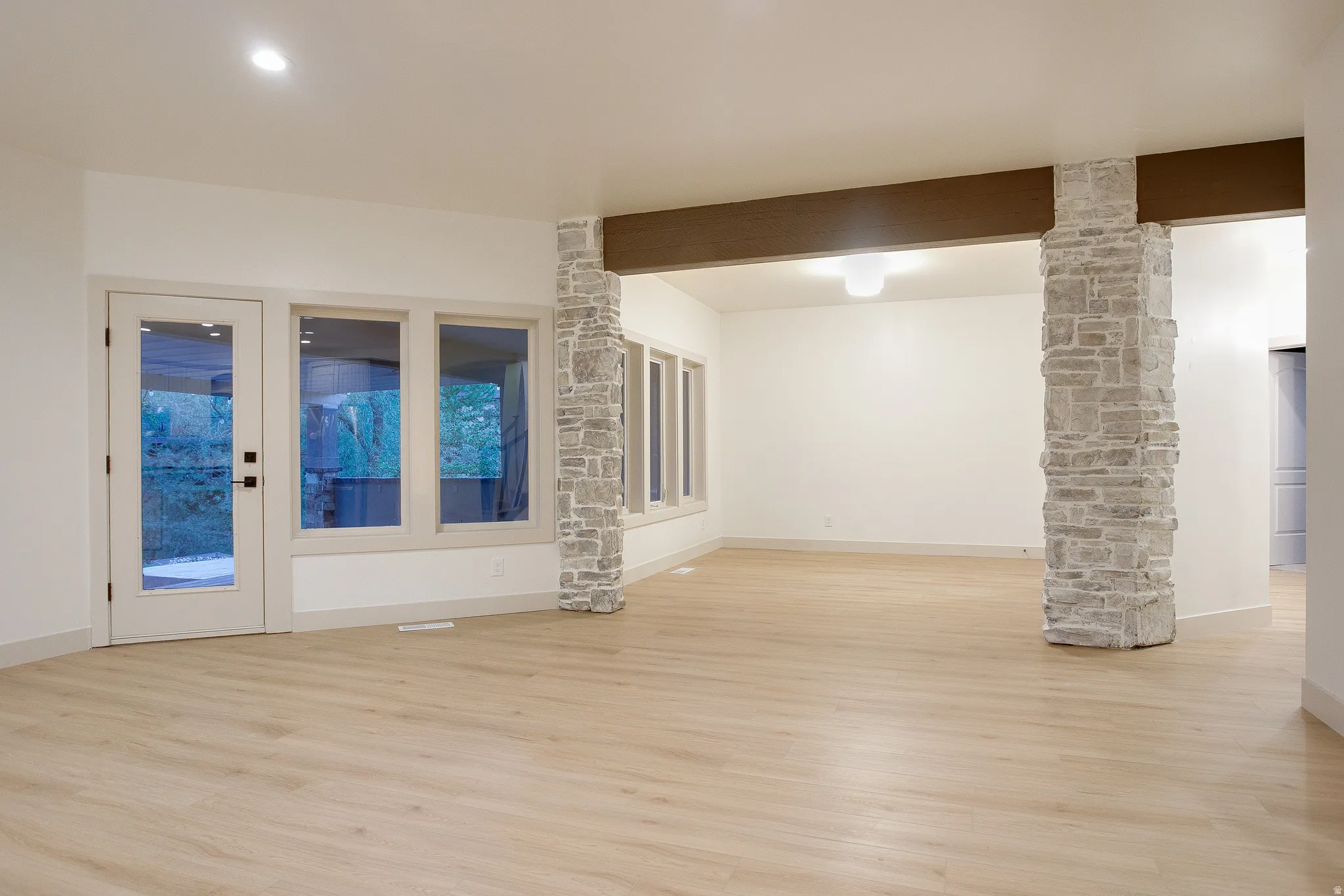 Spacious living area featuring light wood-finish flooring, recessed lighting, and a prominent stone-clad column supporting a wood beam