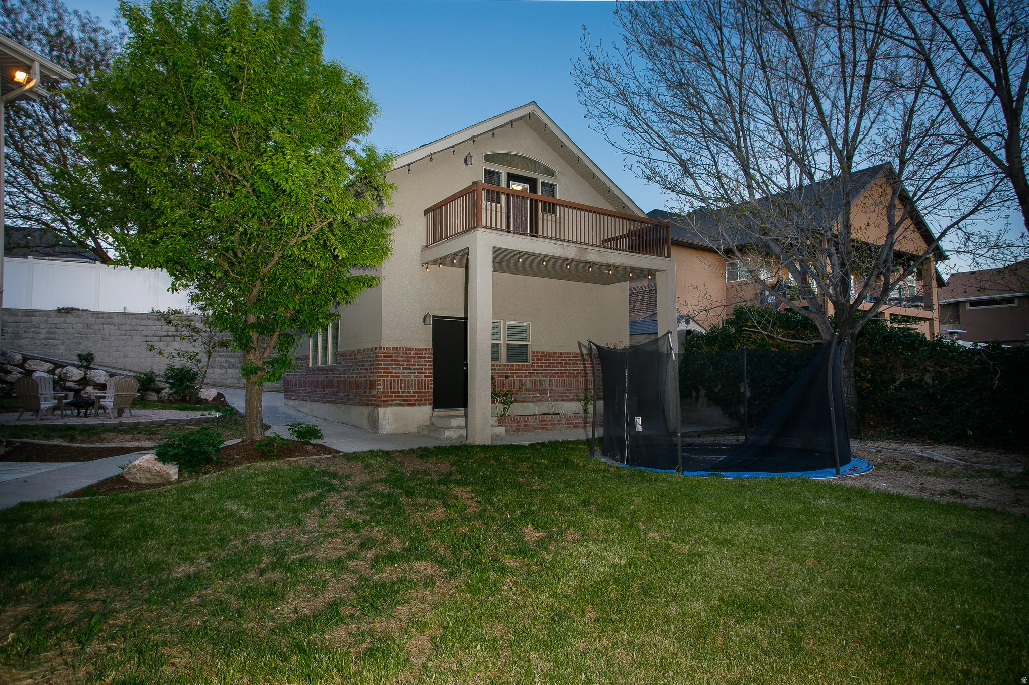 Rear exterior featuring a brick foundation, stucco siding, and a second-story balcony with wood railing