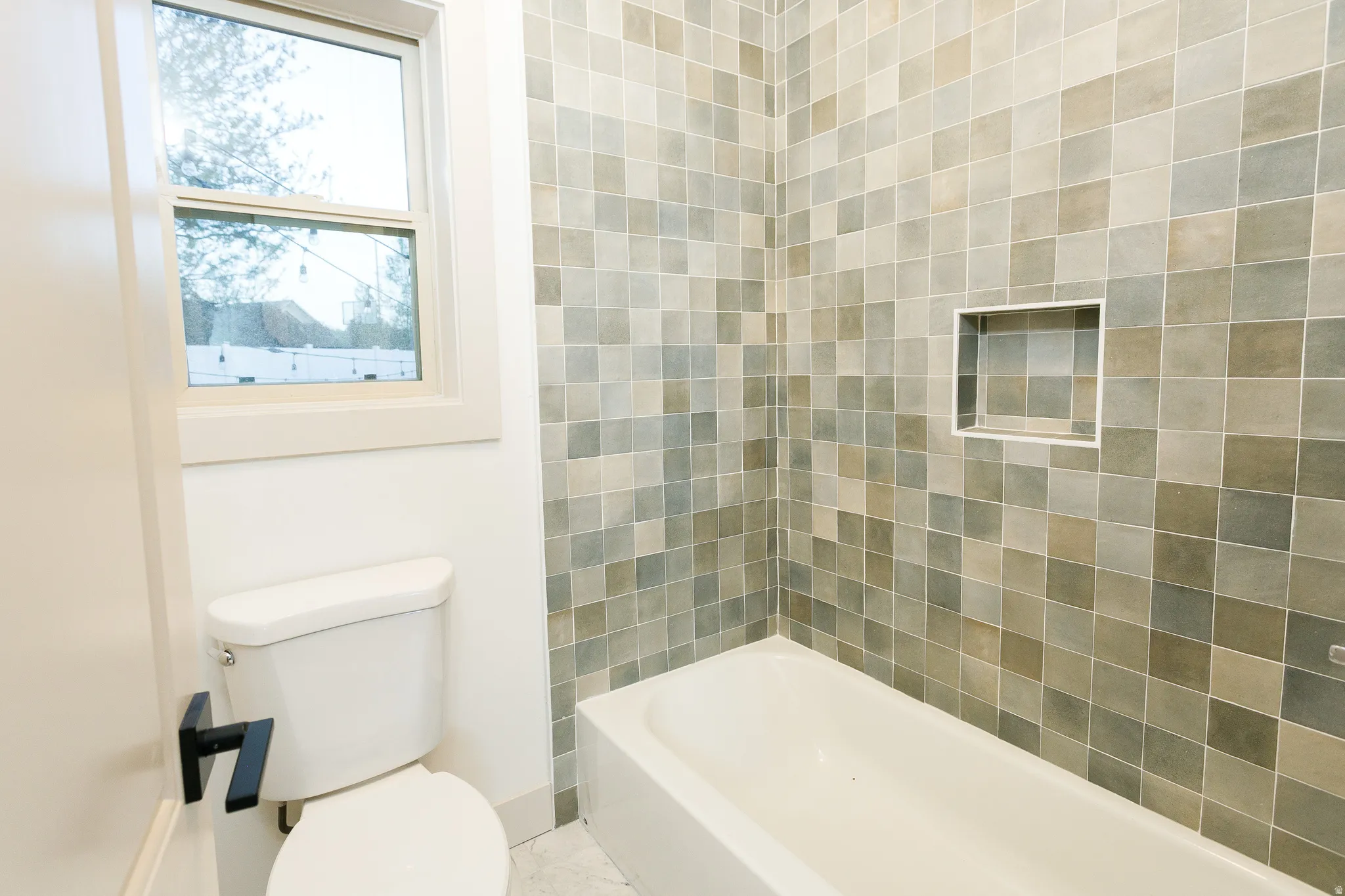 Bathroom featuring a white bathtub, tiled shower surround with an integrated niche, a white toilet, and a window with white trim