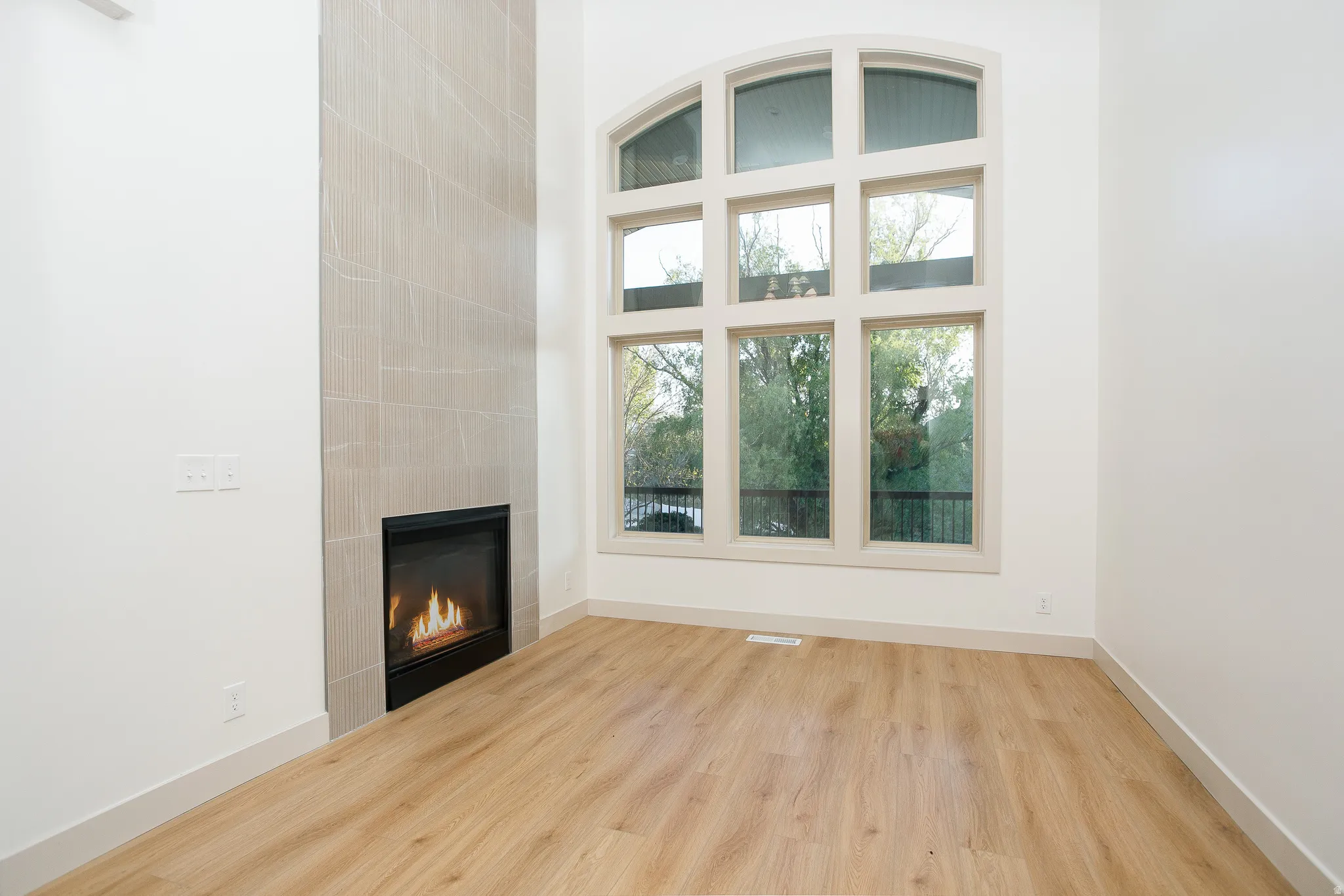 Floor-to-ceiling arched window with multiple panes, wood-finish flooring, and a tiled fireplace surround
