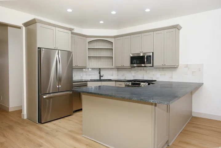 Kitchen featuring a central island with a dark countertop, light-toned cabinetry, stainless steel appliances, a tile backsplash, and wood-finish flooring