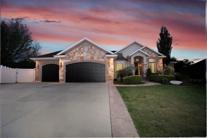Stone and brick facade residence featuring a multi-car garage with arched entrances, a concrete driveway, and a manicured lawn