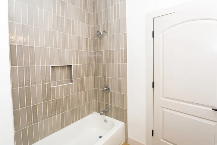 Bathtub with floor-to-ceiling vertical tile surround, integrated shower niche, chrome shower head, and chrome tub faucet
