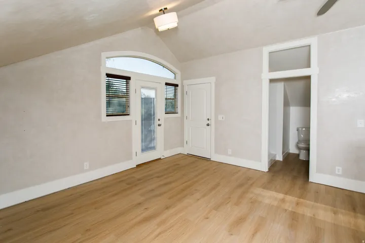 Vaulted ceiling room with wood-finish flooring, a white glass-paneled door, and an arched transom window