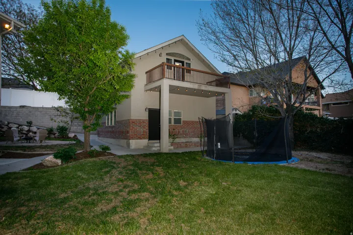 Rear exterior featuring a brick foundation, stucco siding, and a second-story balcony with wood railing